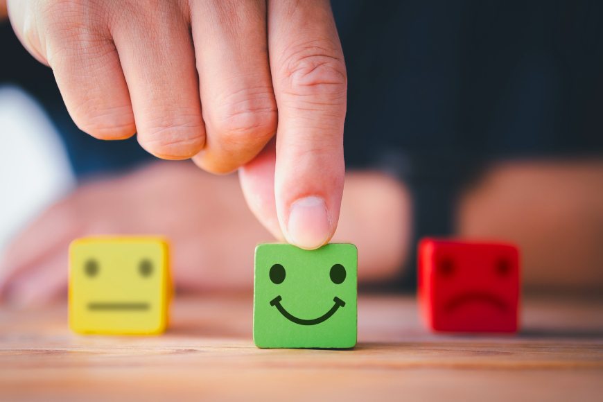 Close up of coloured wooden toy blocks in green, red and yellow, with happy, sad and neutral faces