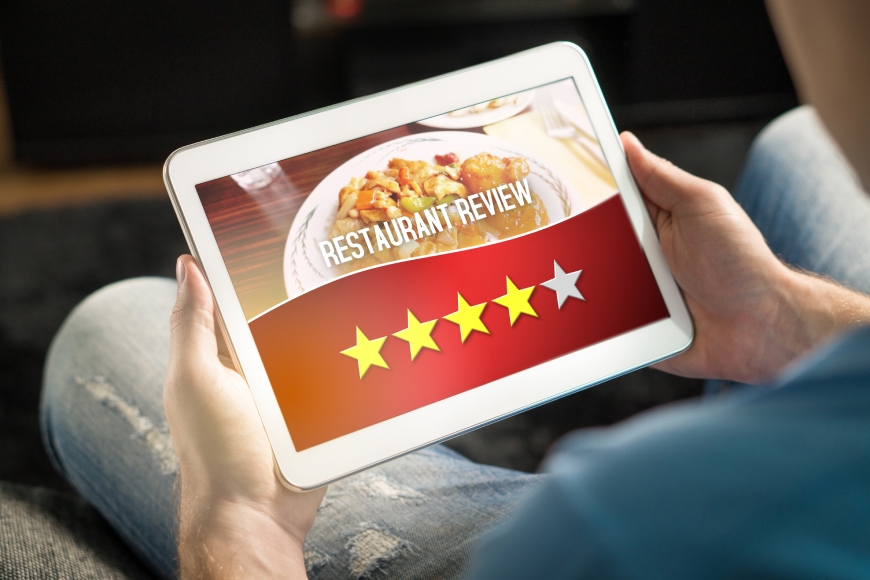 Hands holding iPad tablet showing restaurant review on screen, 4 out of 5 star rating