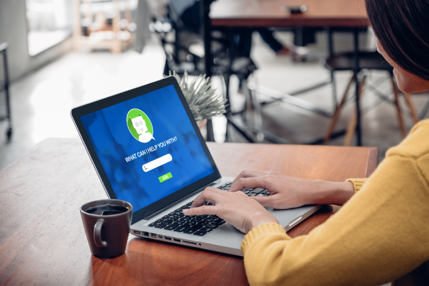 Woman sitting at desk typing on laptop using chatbot