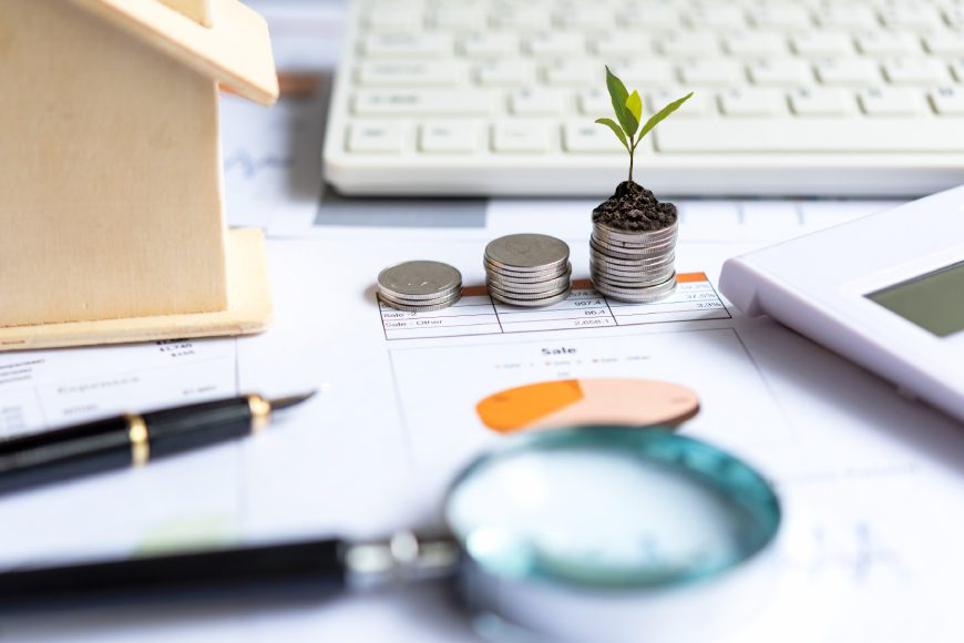 Stacks of money coins on desk with magnifying glass