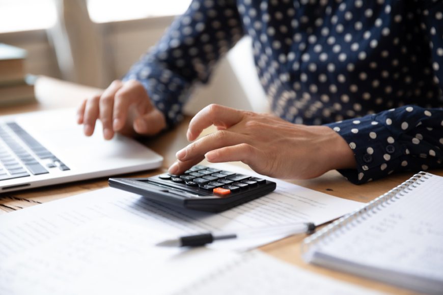 Hands typing numbers on calculator beside laptop on desk