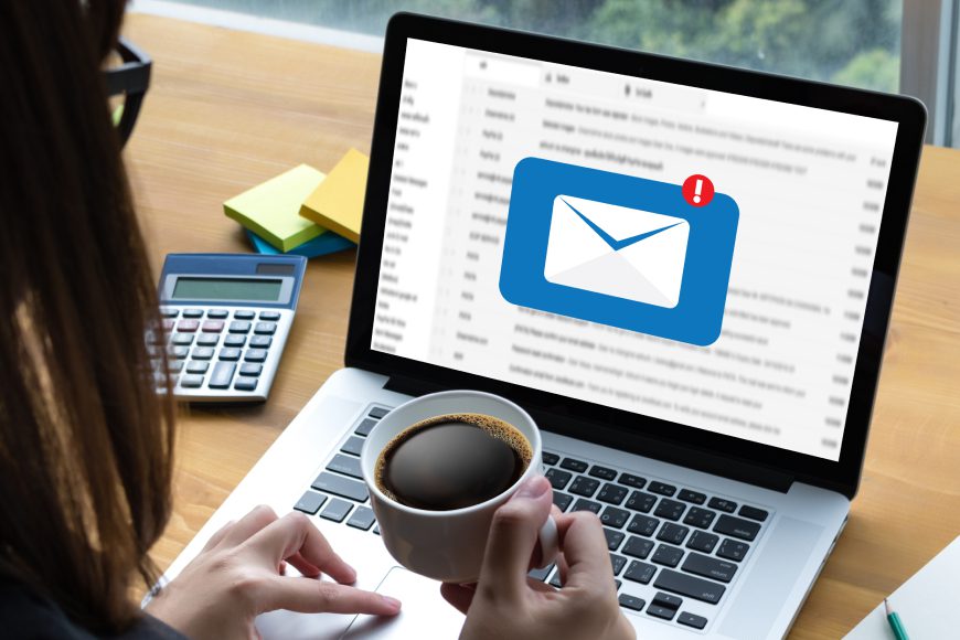 Woman holding coffee cup and using laptop with inbox message notification on screen