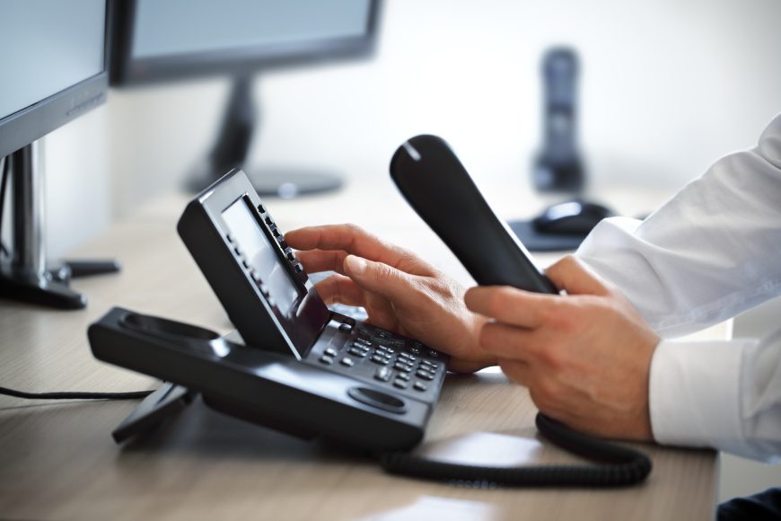 Hands holding landline phone and dialling numbers on key pad