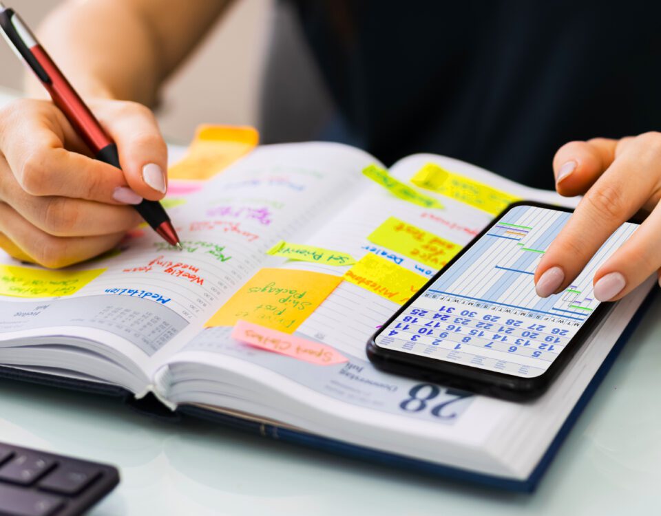 Hands using pen and phone to add calendar dates to diary