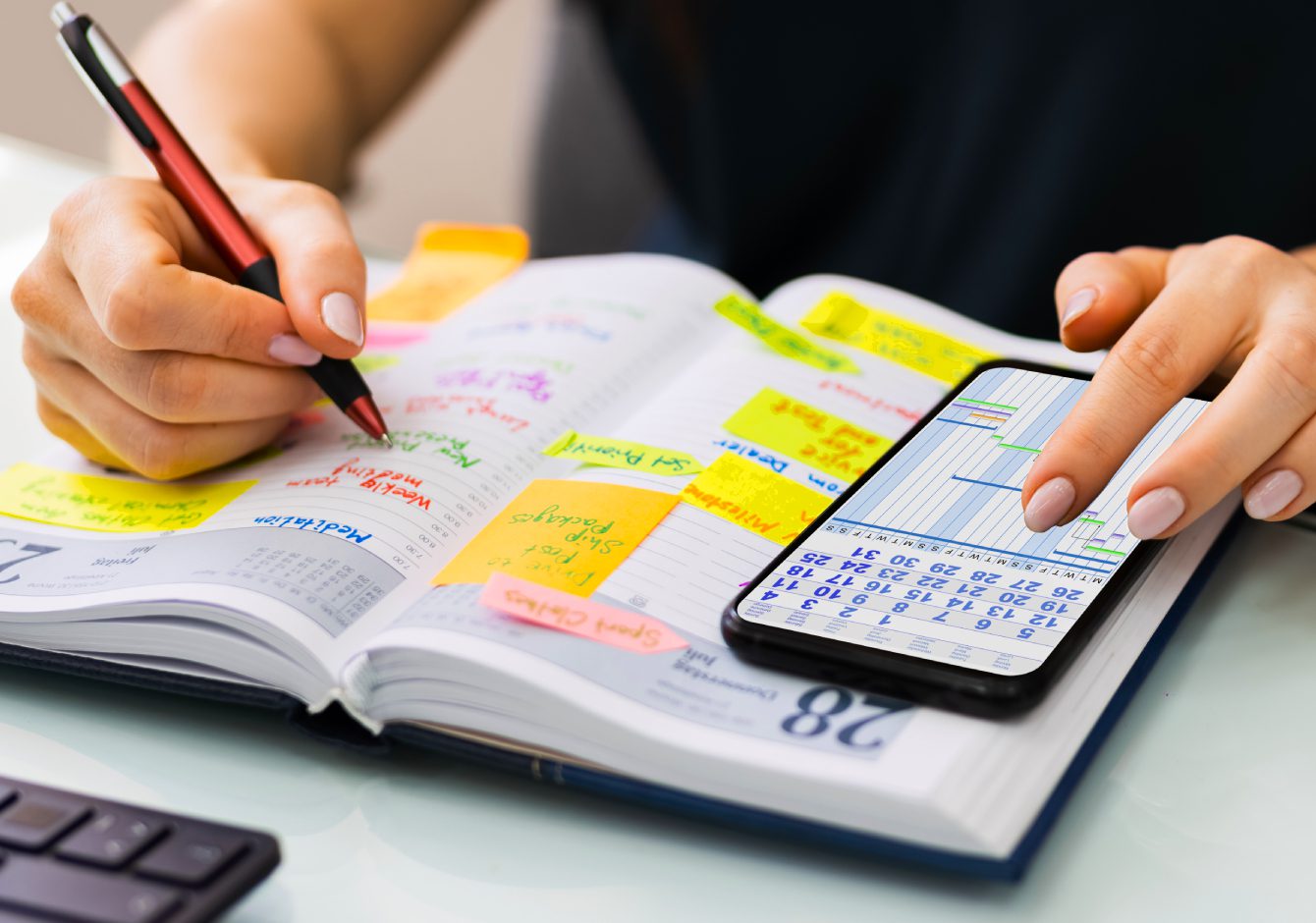 Hands using pen and phone to add calendar dates to diary