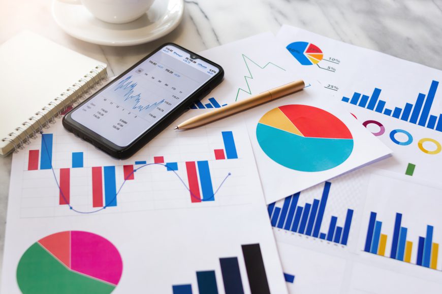 Graphs and charts on paper beside smartphone on desk