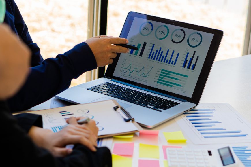 People pointing at laptop with charts on screen