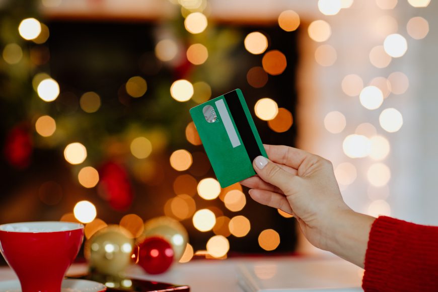 Woman's hand holding green credit card against glowing Christmas lights in the background