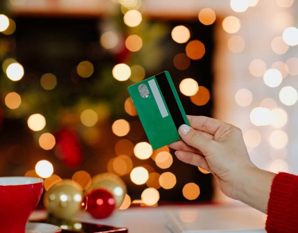 Woman's hand holding green credit card against glowing Christmas lights in the background