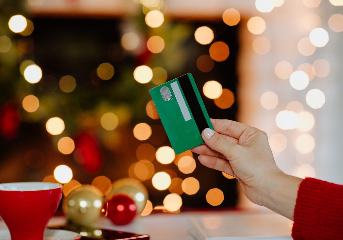 Woman's hand holding green credit card against glowing Christmas lights in the background