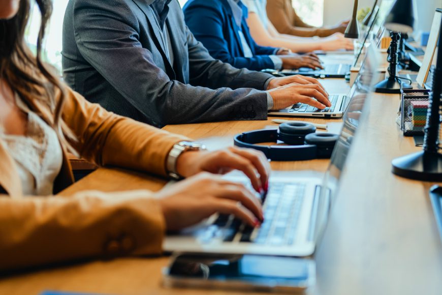 Row of team members sitting at desk in office typing on computers