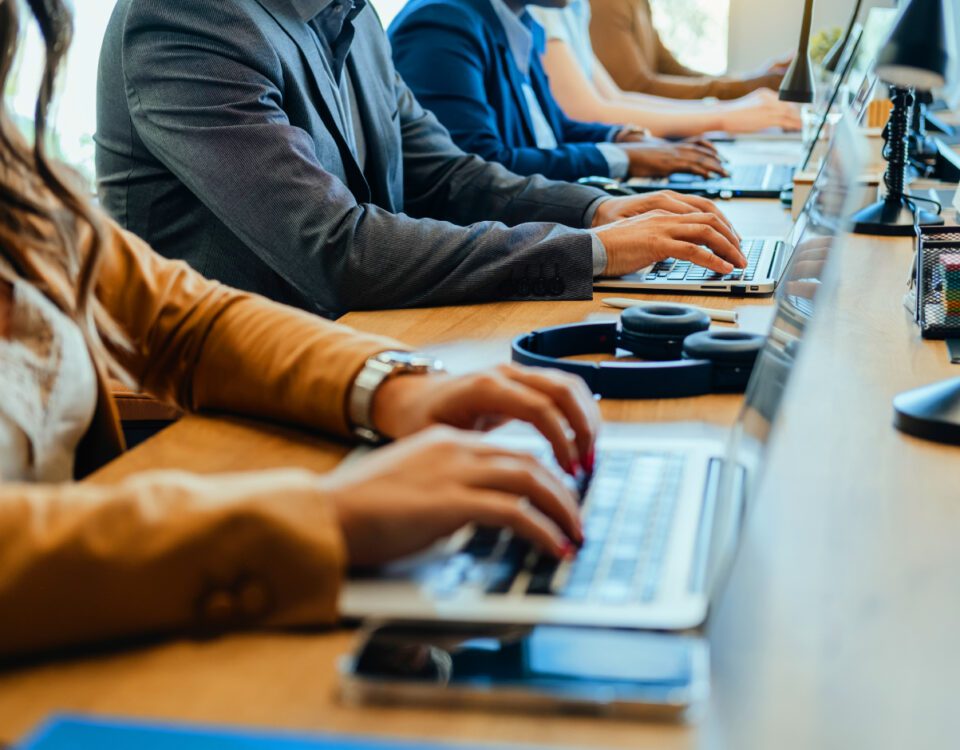 Row of team members sitting at desk in office typing on computers