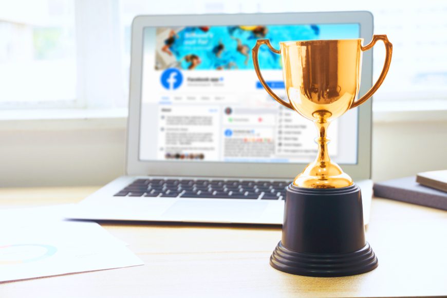 Gold trophy beside laptop with Facebook on screen