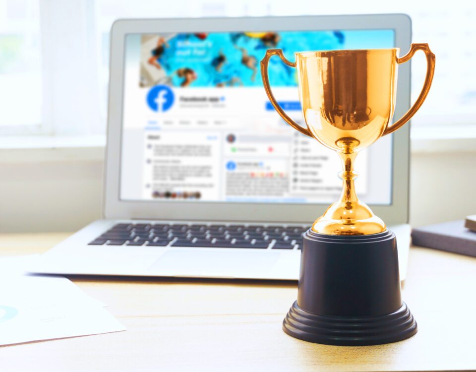 Gold trophy beside laptop with Facebook on screen