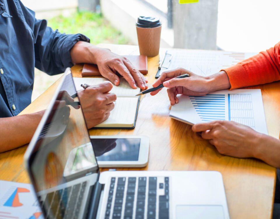 Coworkers discussing marketing ideas at desk with tablet and laptop