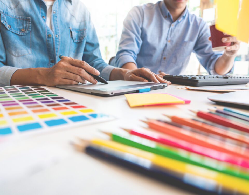 Pencils and colour swatches on desk with graphic designer using tablet