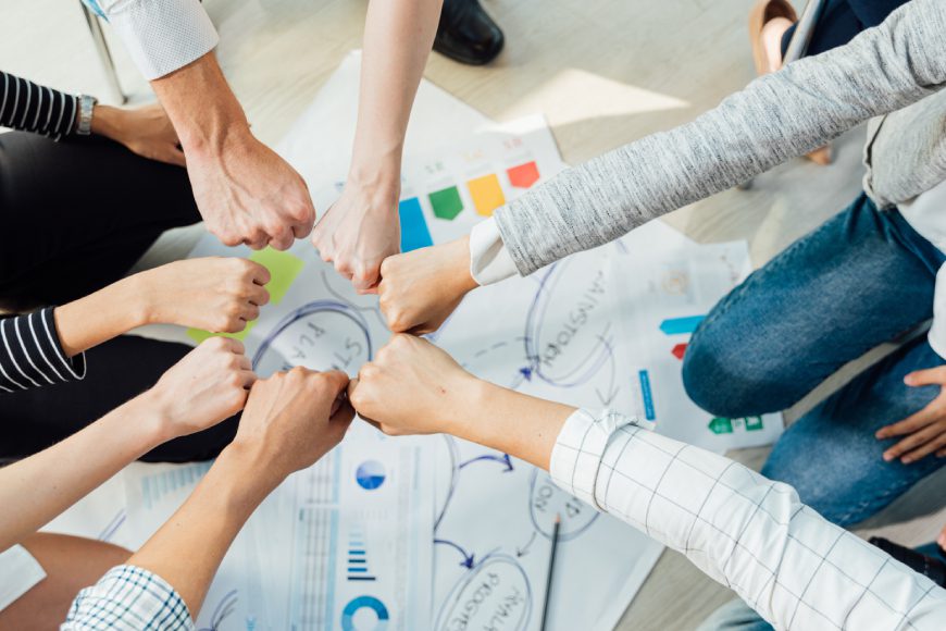 Team members putting their hands together with graphs and charts on paper in background