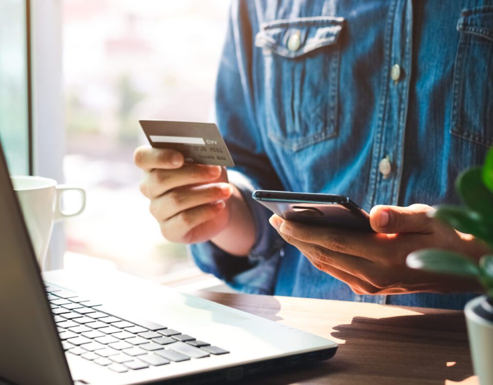 Person holding credit card and using smartphone in front of laptop