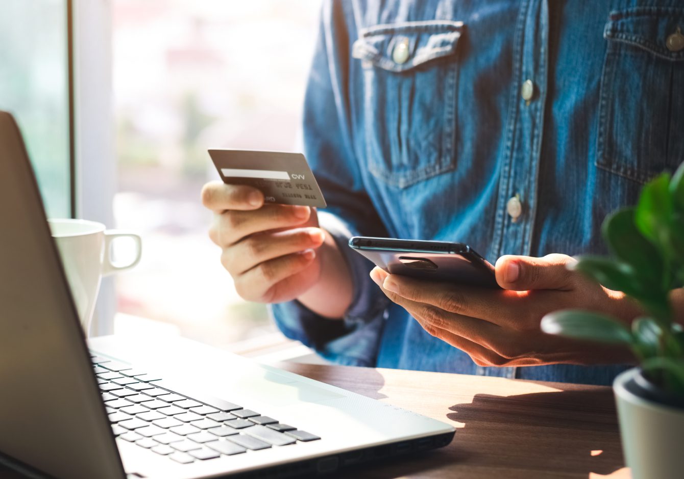 Person holding credit card and using smartphone in front of laptop