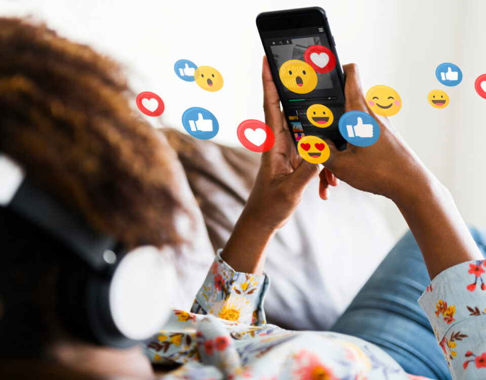 Hands holding smartphone with social media reaction emoji icons around screen