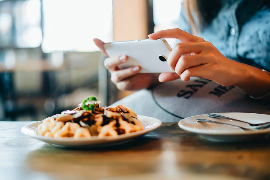 Hands holding smartphone taking photo of restaurant food dishes