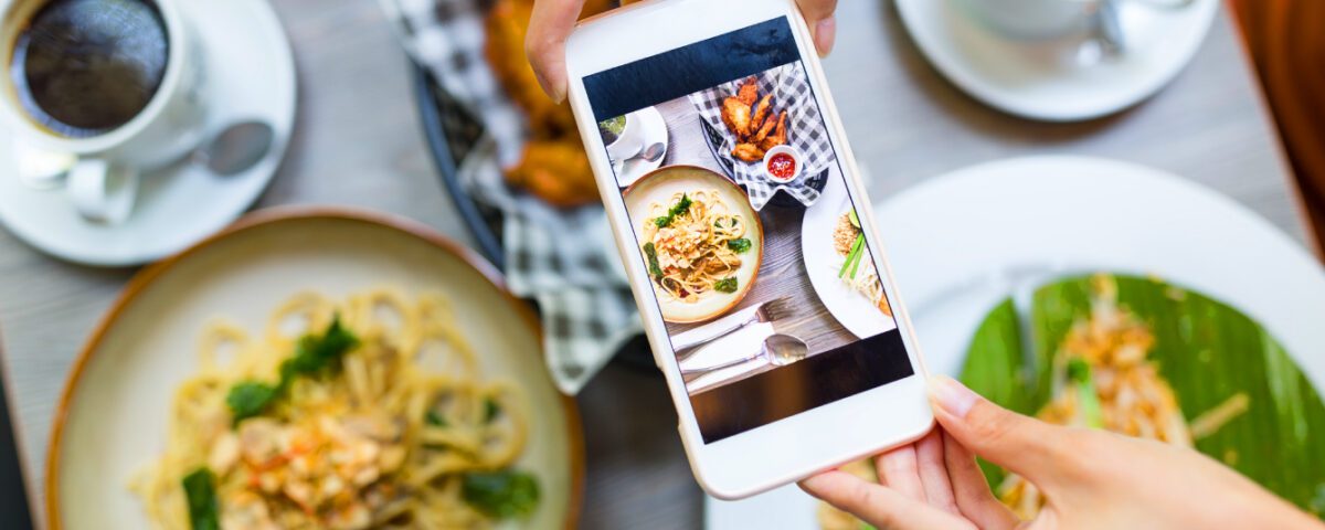 Hands holding smartphone taking photo of restaurant food dishes