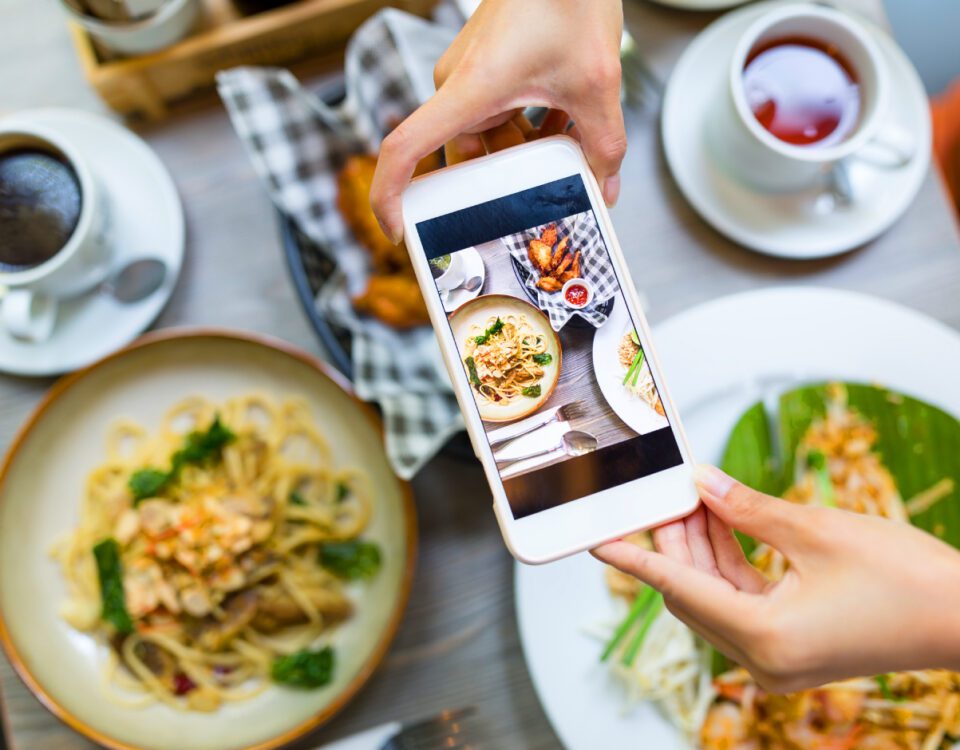 Hands holding smartphone taking photo of restaurant food dishes