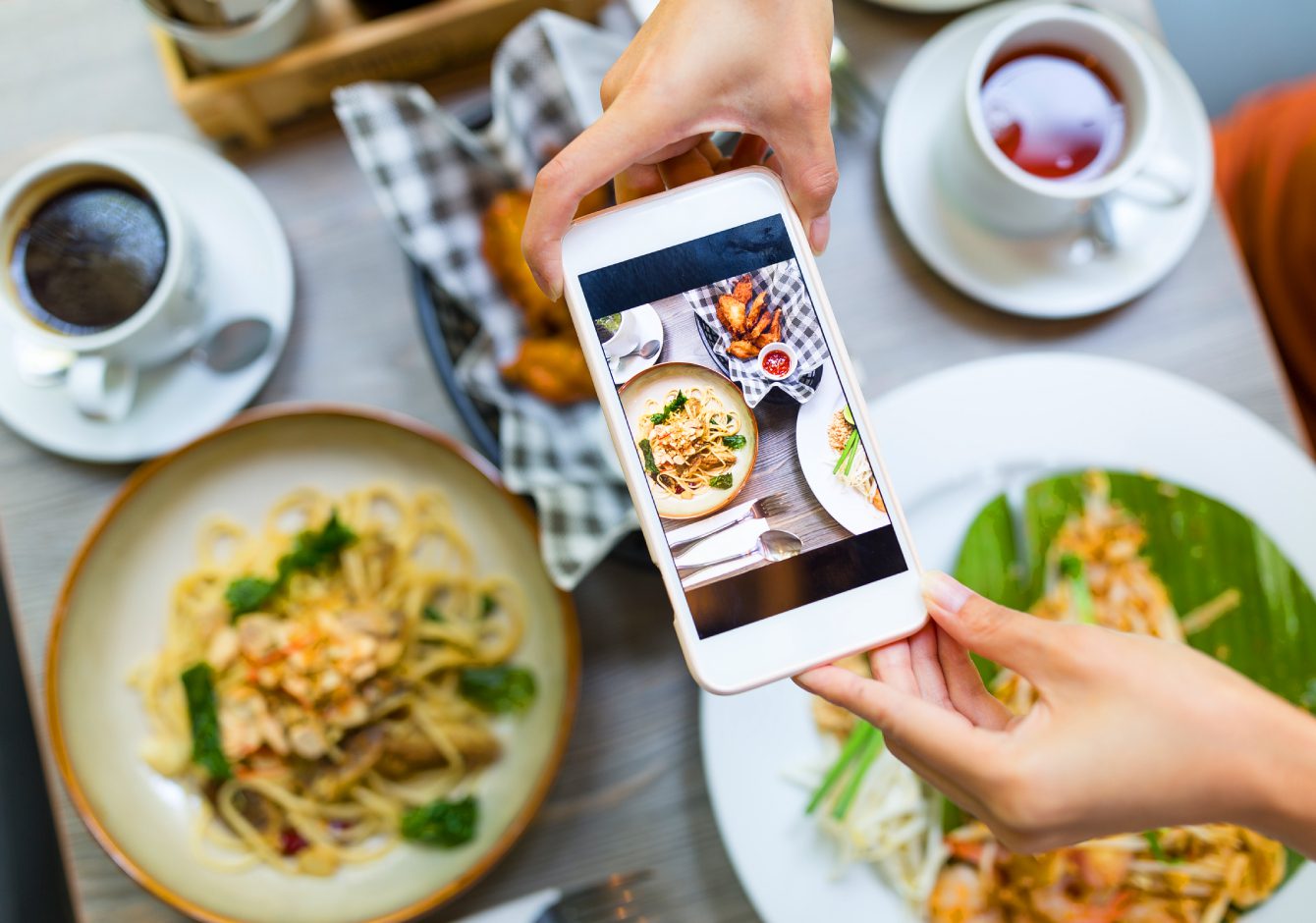 Hands holding smartphone taking photo of restaurant food dishes