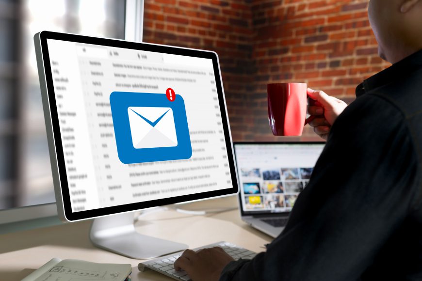 Person sitting at desk with cup of coffee looking at desktop computer with inbox notification on screen