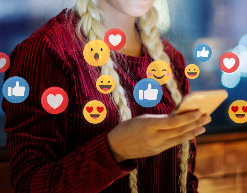Woman with blonde hair in braids holding smartphone with social media emoji reactions around it
