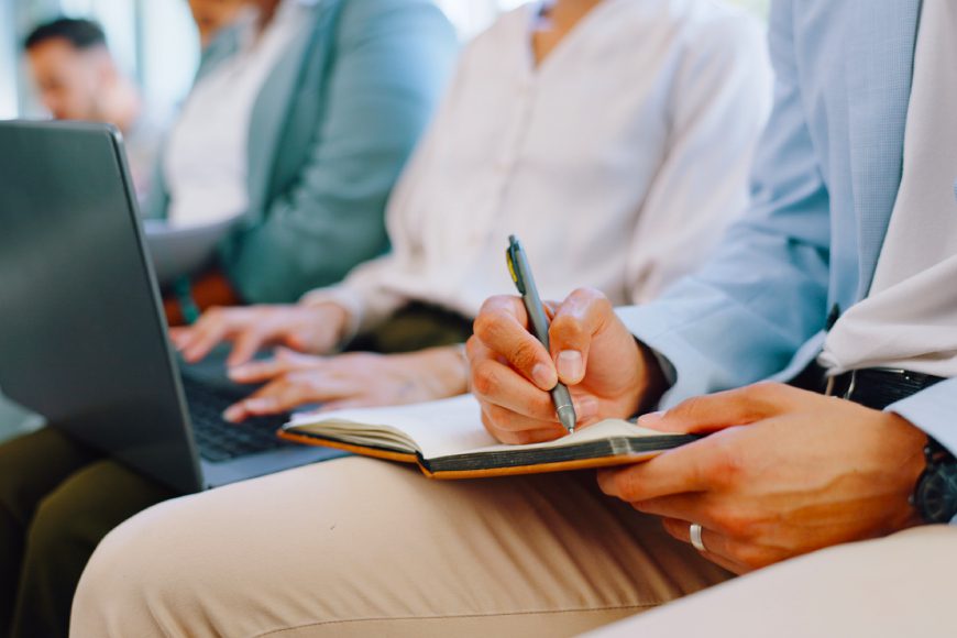 Office people sitting in a row typing on laptop and writing in notebook