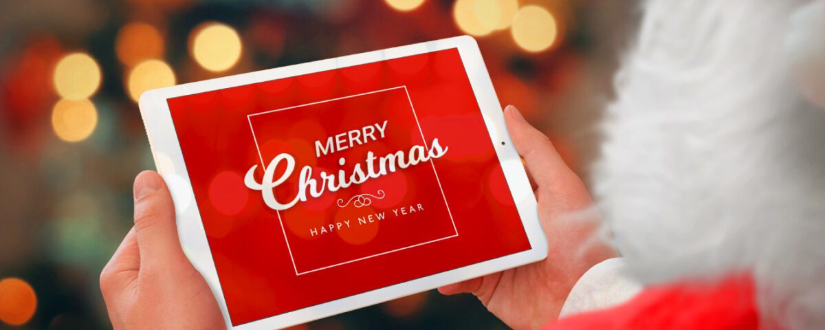 Santa Claus holding iPad tablet in front of Christmas lights with festive message on screen
