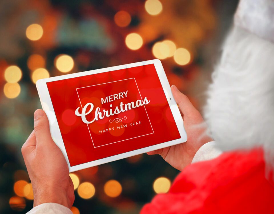 Santa Claus holding iPad tablet in front of Christmas lights with festive message on screen