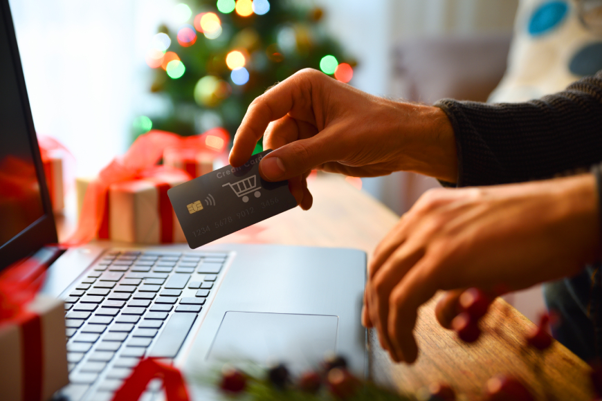 Person using laptop with credit card and Christmas gifts in background