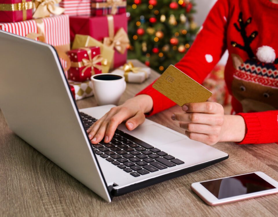 Person using laptop with credit card and Christmas gifts in background