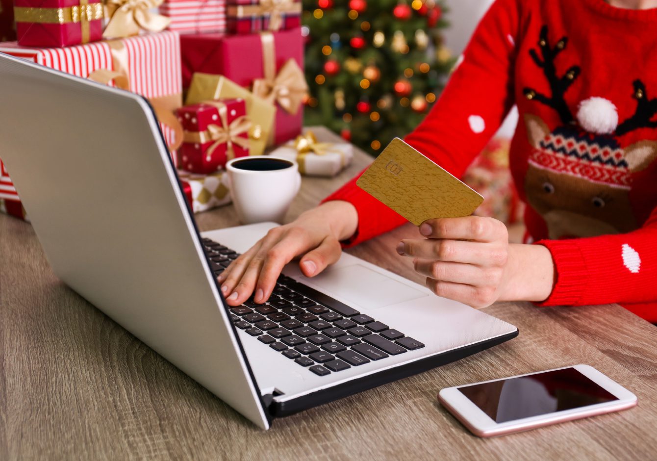 Person using laptop with credit card and Christmas gifts in background