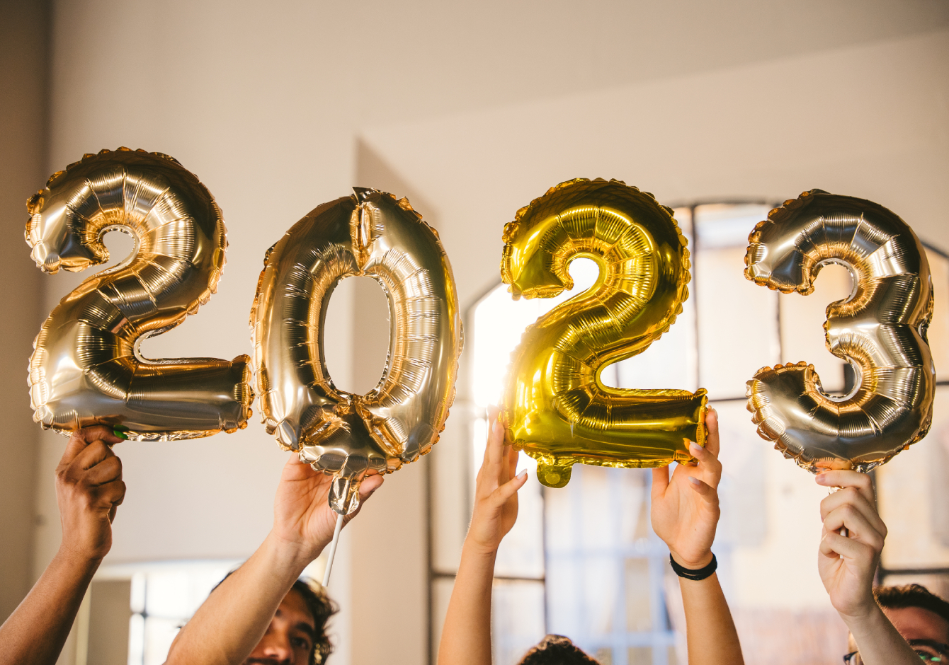 Hands holding gold number balloons that spell out 2023