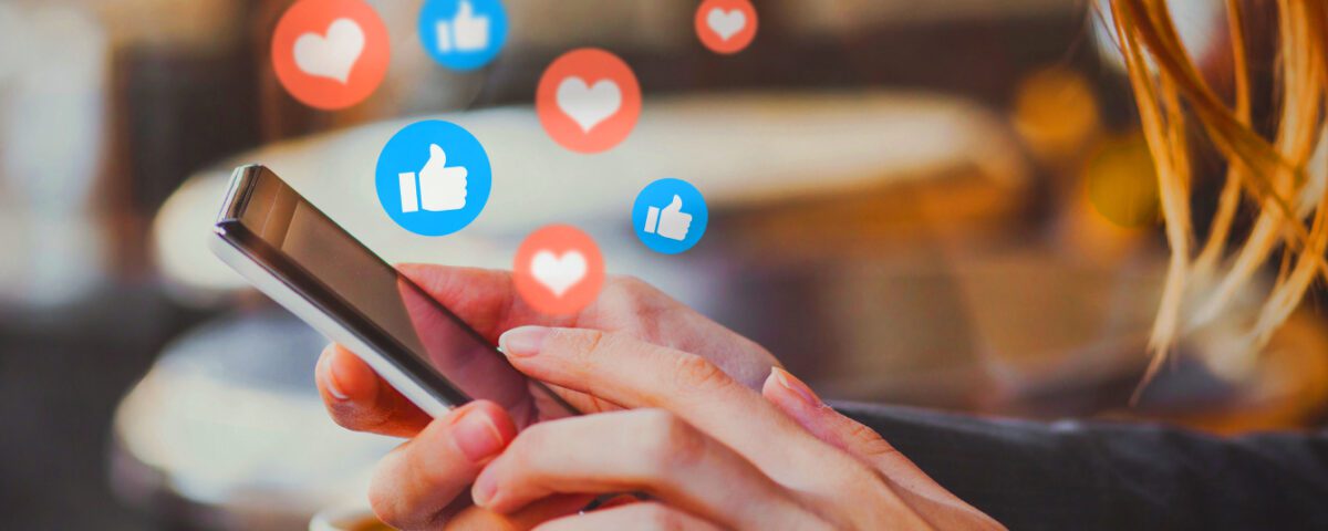 Hands holding smartphone with social media hearts and thumbs up icons