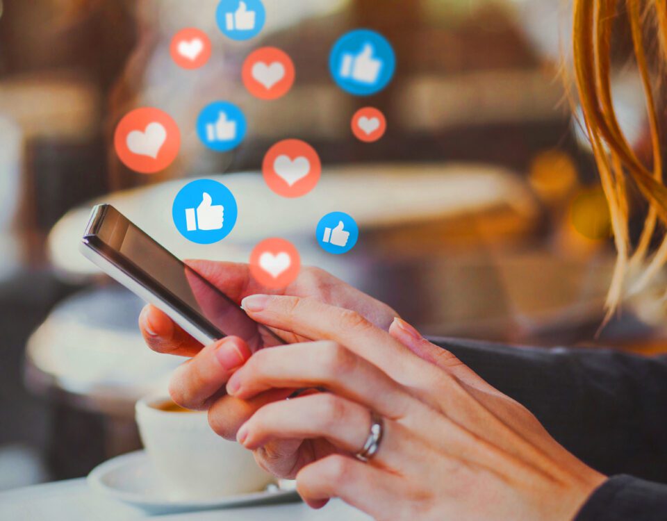 Hands holding smartphone with social media hearts and thumbs up icons