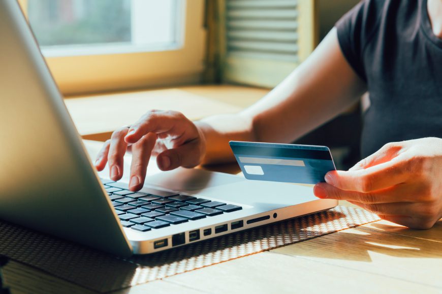 Hands holding credit card while typing on laptop