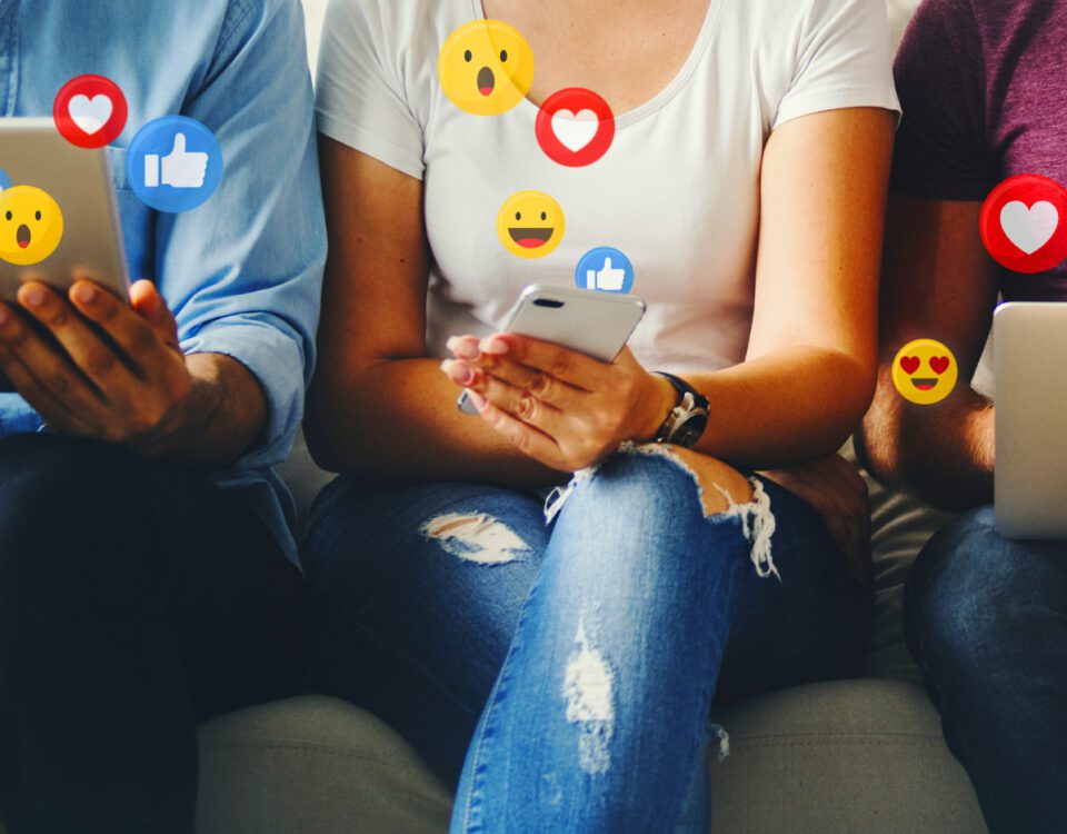 People using devices with social media emoji reactions around them