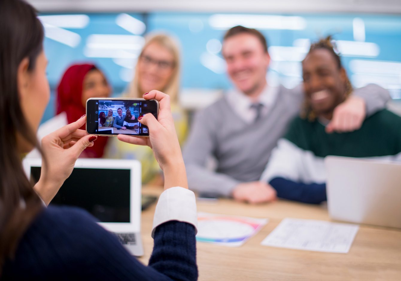 Woman using smartphone to take photo of team members in office