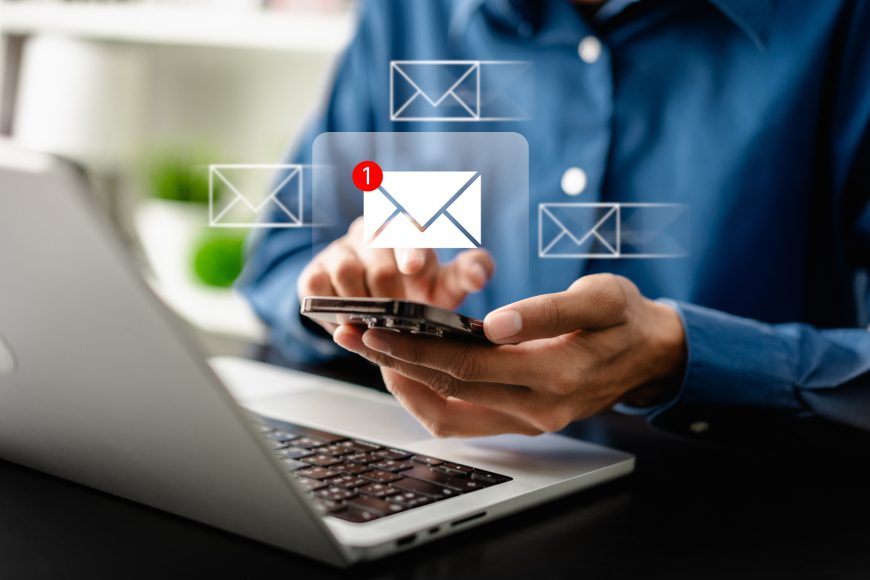 Hands holding smartphone in front of laptop with message notifications