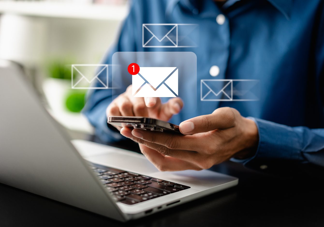 Hands holding smartphone in front of laptop with message notifications