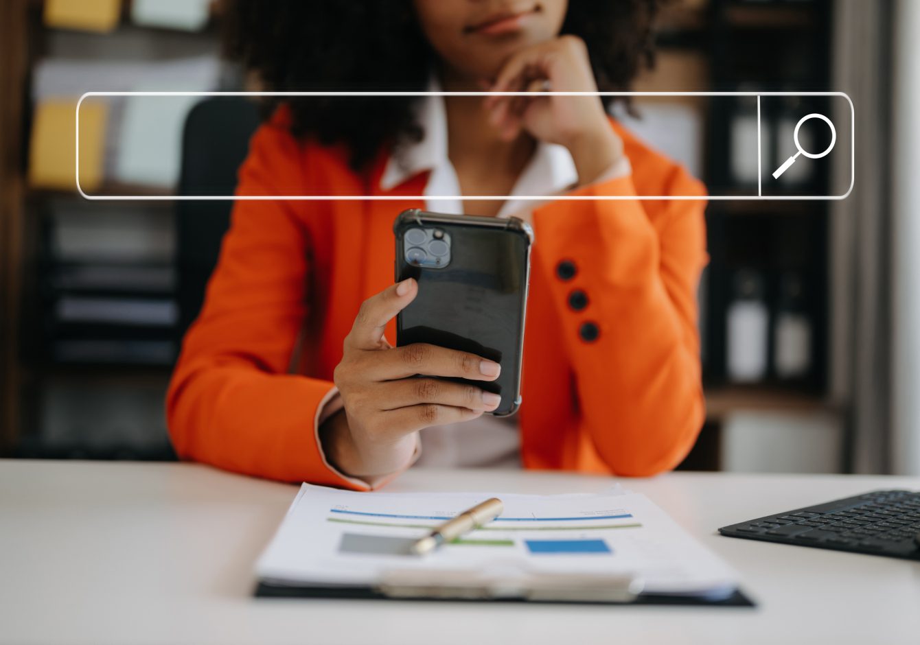 Woman sitting at desk using smartphone with search bar