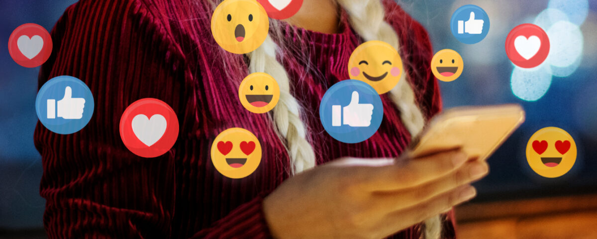 Woman holding smartphone with social media reaction emojis around it