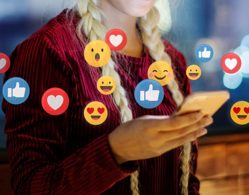 Woman holding smartphone with social media reaction emojis around it