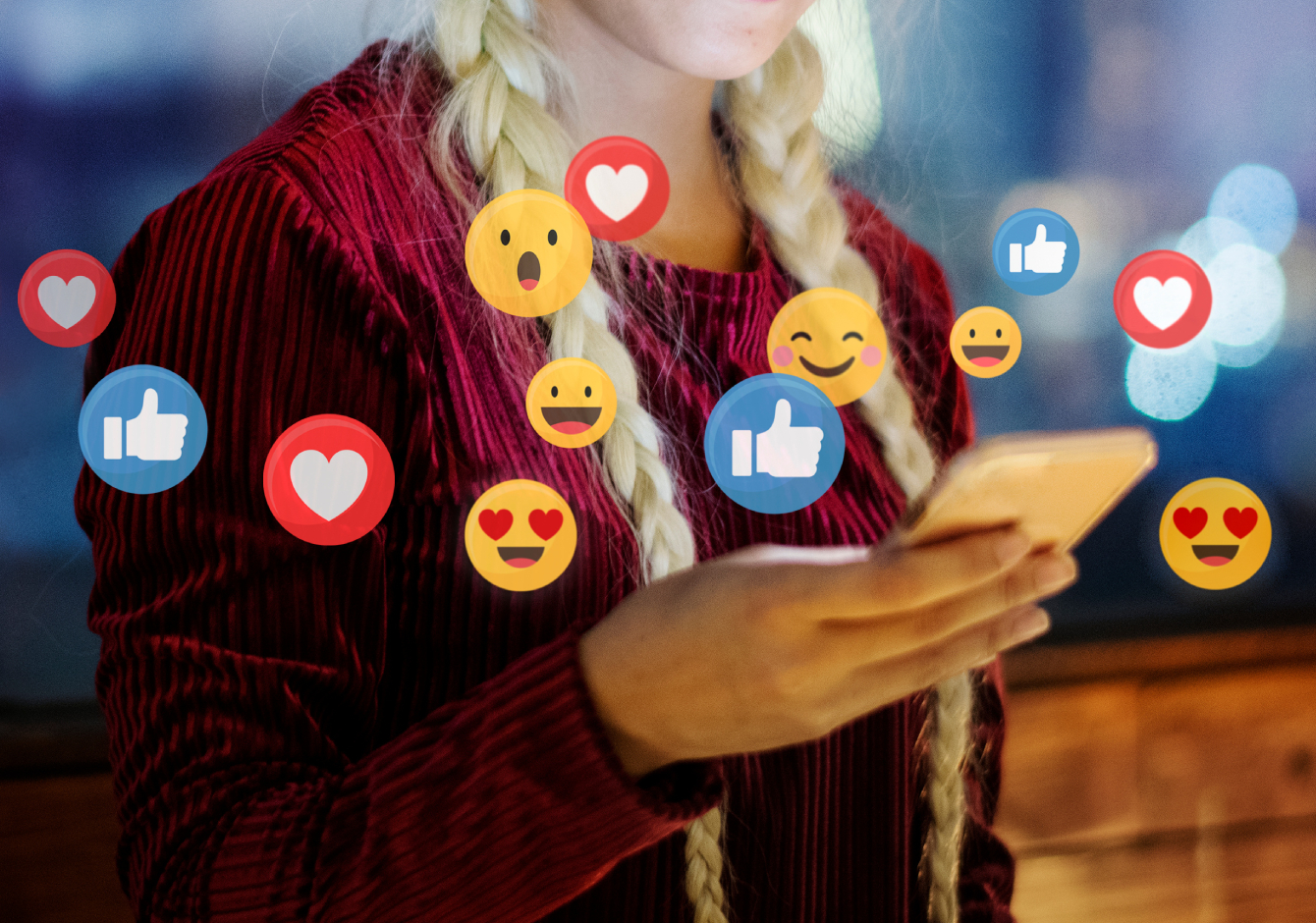 Woman holding smartphone with social media reaction emojis around it