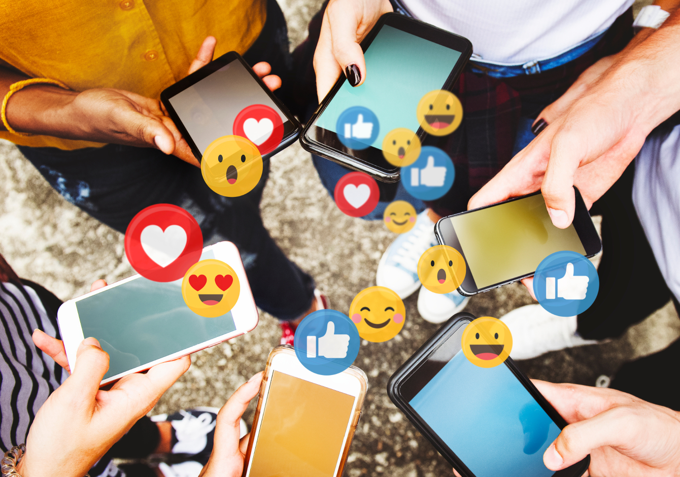 Friends standing in a circle holding smartphones with social media reaction emojis around