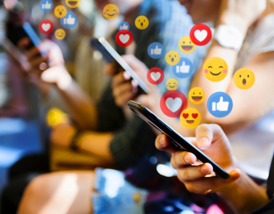 Row of people using smartphones with social media reaction emojis around